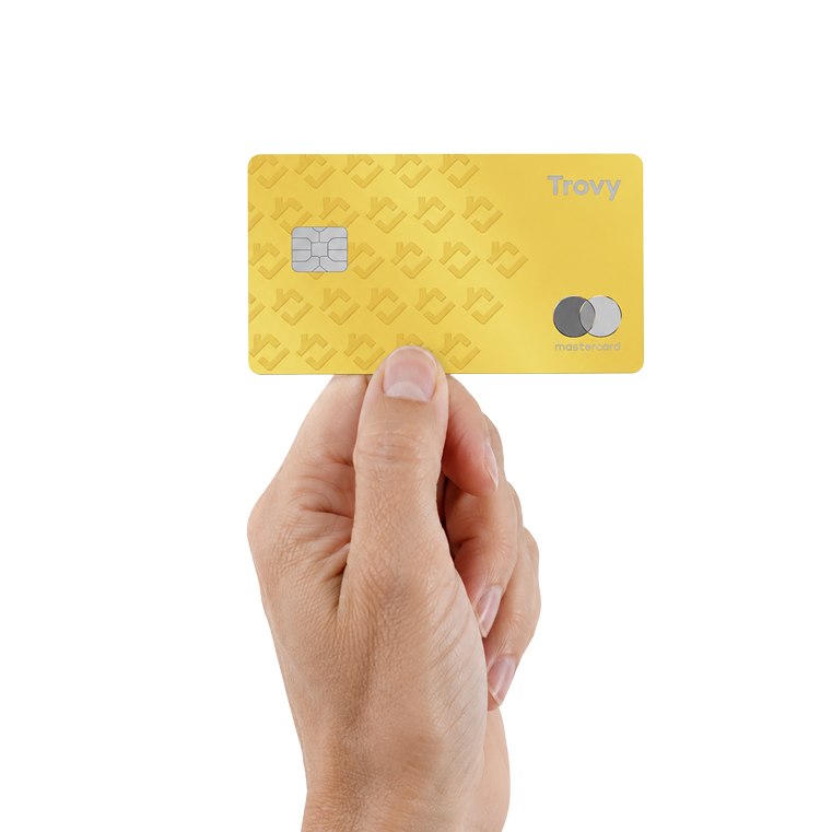 A hand holding the gold Trovy Card in front of a home