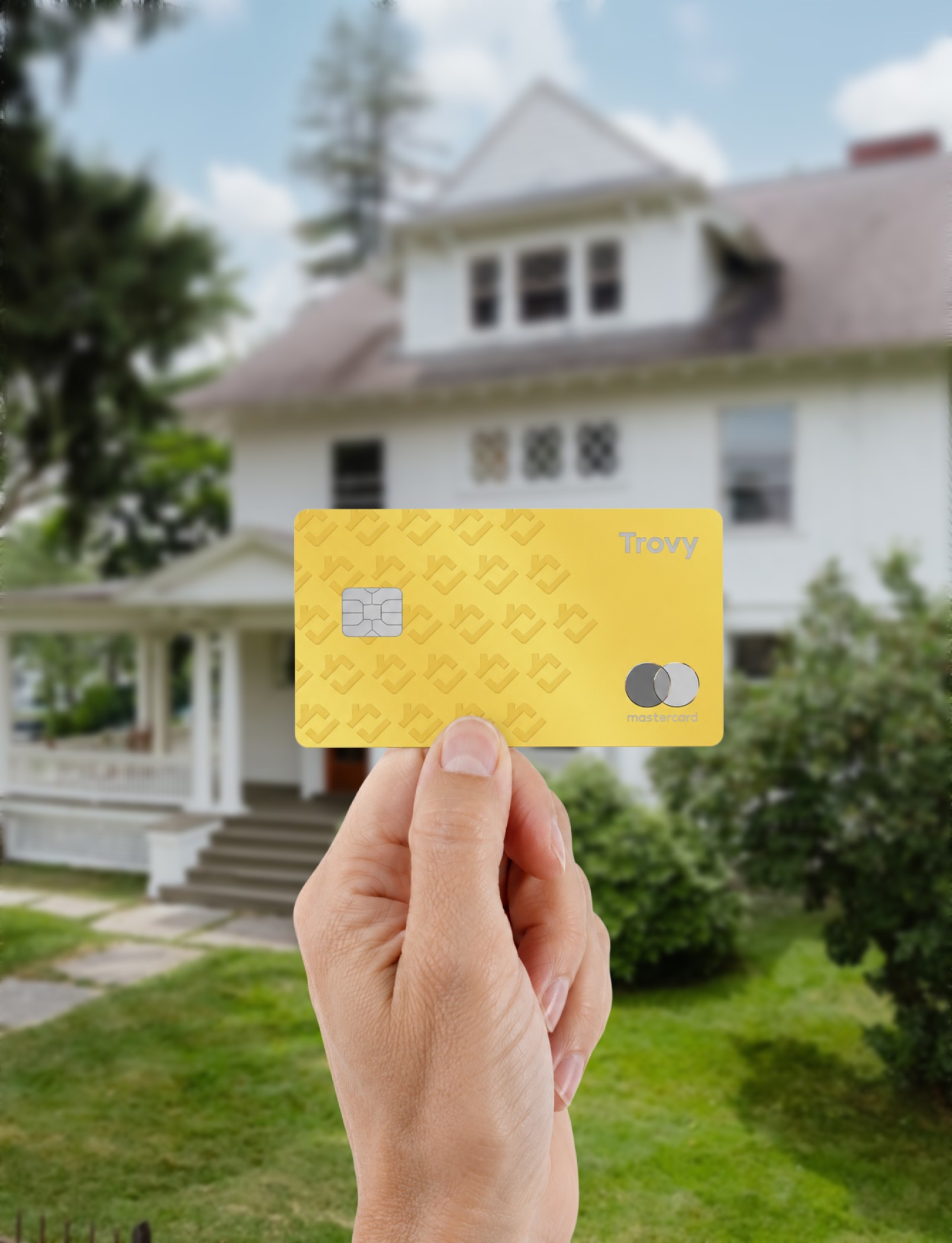 A hand holding a Trovy HELOC credit card in front of a home